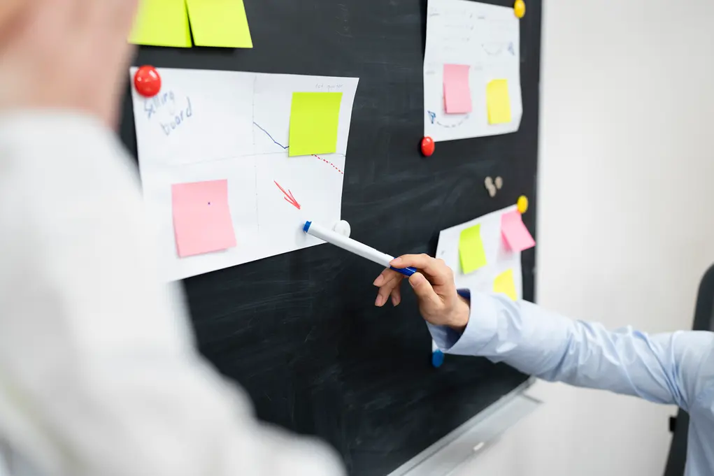 Imagem de pessoa apontando caneta para papel fixado em quadro negro ilustrando painel de gestão de à vista.
