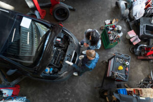 imagem de cima de um pátio da oficina com mecânico, cliente e um carro com o capô aberto.