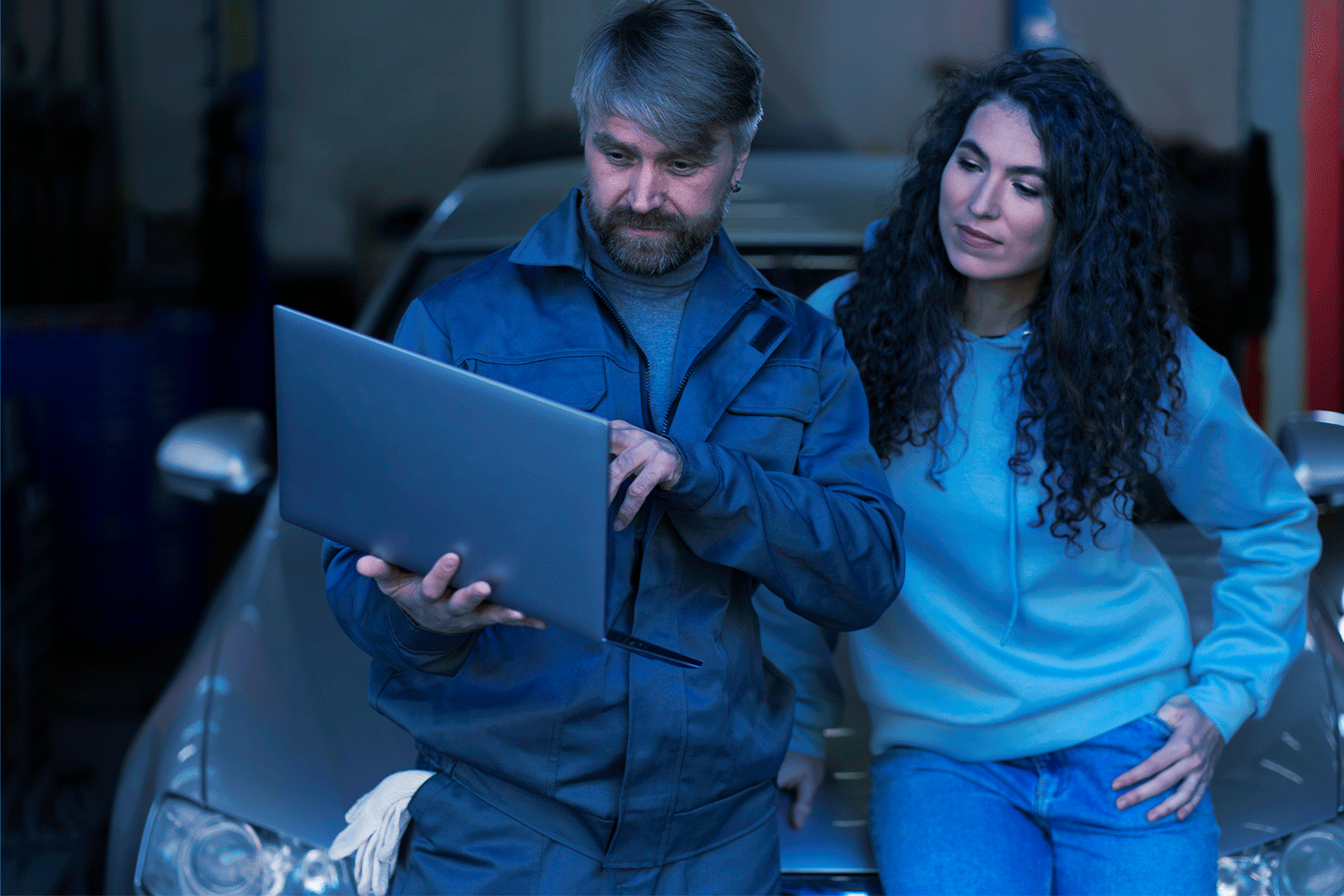 Gestor de oficina em frente a um carro segurando um notebook, ao lado de uma cliente.
