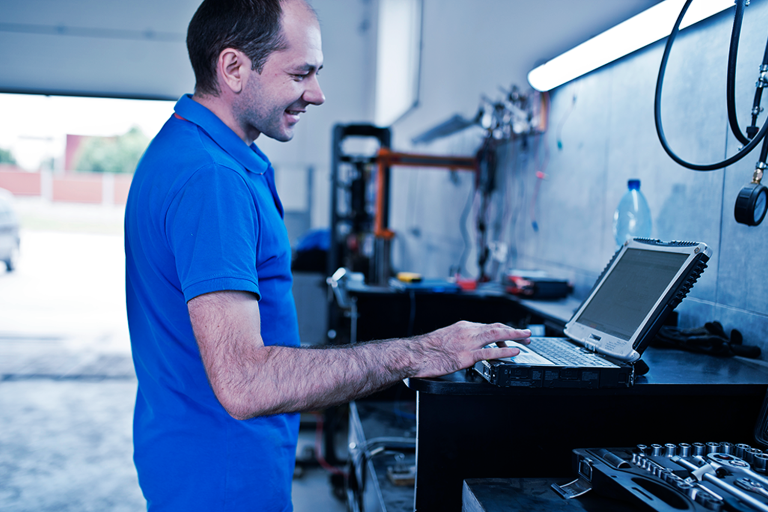 Gestor no pátio da oficina olhando para um computador e sorrindo.