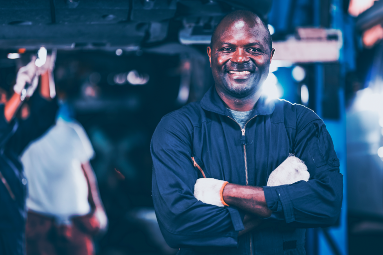 Mecânico de braços cruzados e sorrindo no pátio da oficina