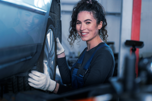 Mecânica sorrindo para segurando a roda do carro.